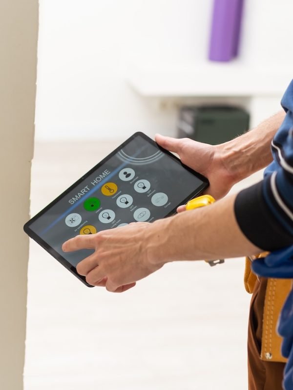 electrician in hardhat and safety vest holding digital tablet and fixing electric panel.